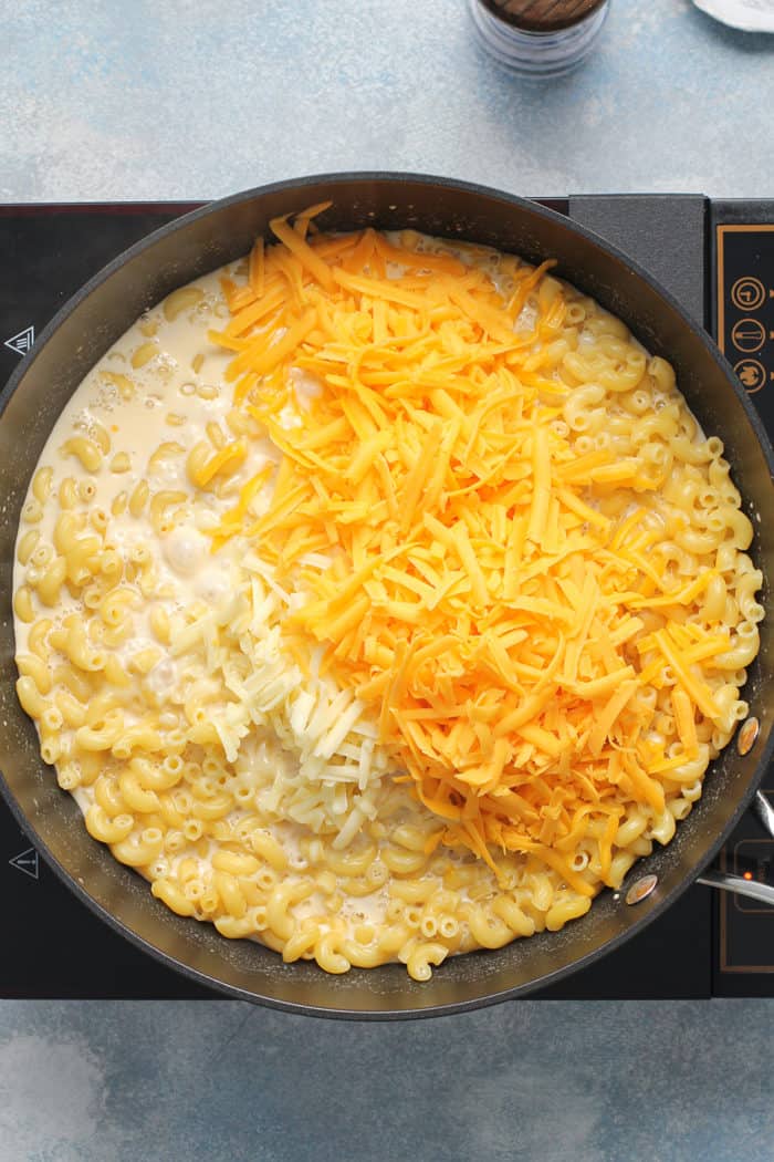 Shredded cheddar cheese being added to a pot of macaroni