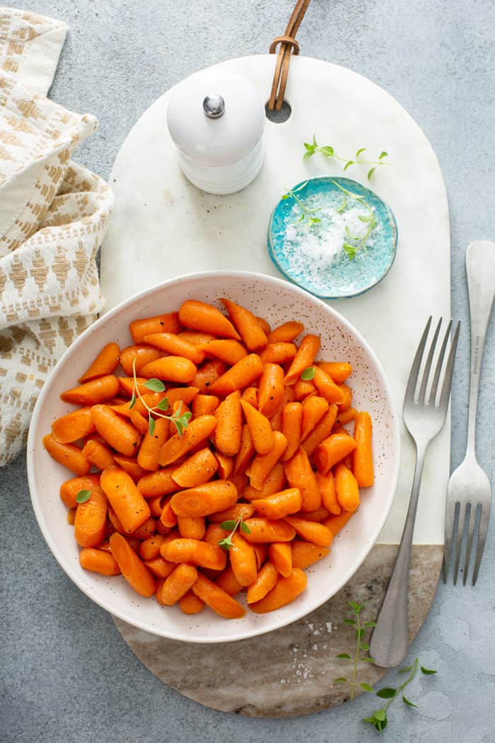 Overhead view of a white bowl filled with honey glazed carrots on a marble board