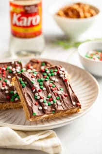 Plated peanut butter pretzel bars with corn syrup and a bowl of pretzels in the background