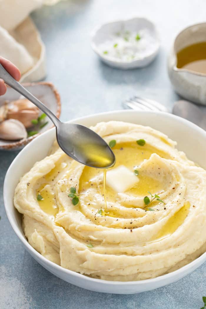 Spoon drizzling melted butter over a bowl of garlic mashed potatoes