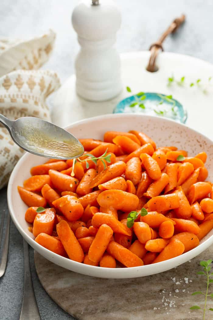 Spoon drizzling honey glaze over cooked carrots in a white bowl