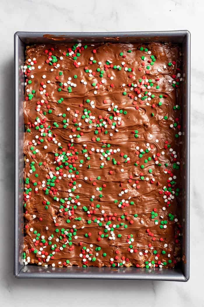 Overhead view of peanut butter pretzel bars topped with red and green sprinkles in a metal baking pan