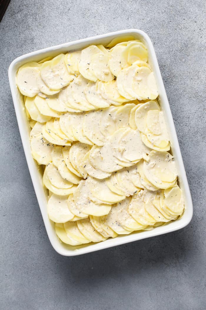 Sliced potatoes and cream sauce layered in a white baking dish, ready to bake