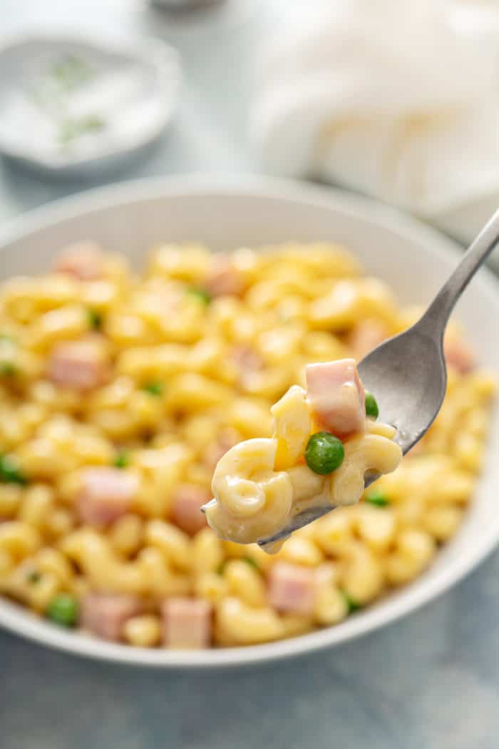 Fork holding a bite of mac and cheese with ham and peas mixed in