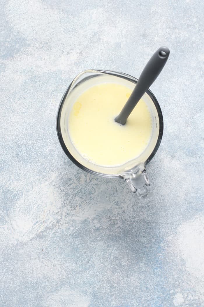 Butter and heavy cream in a glass measuring cup on a blue countertop