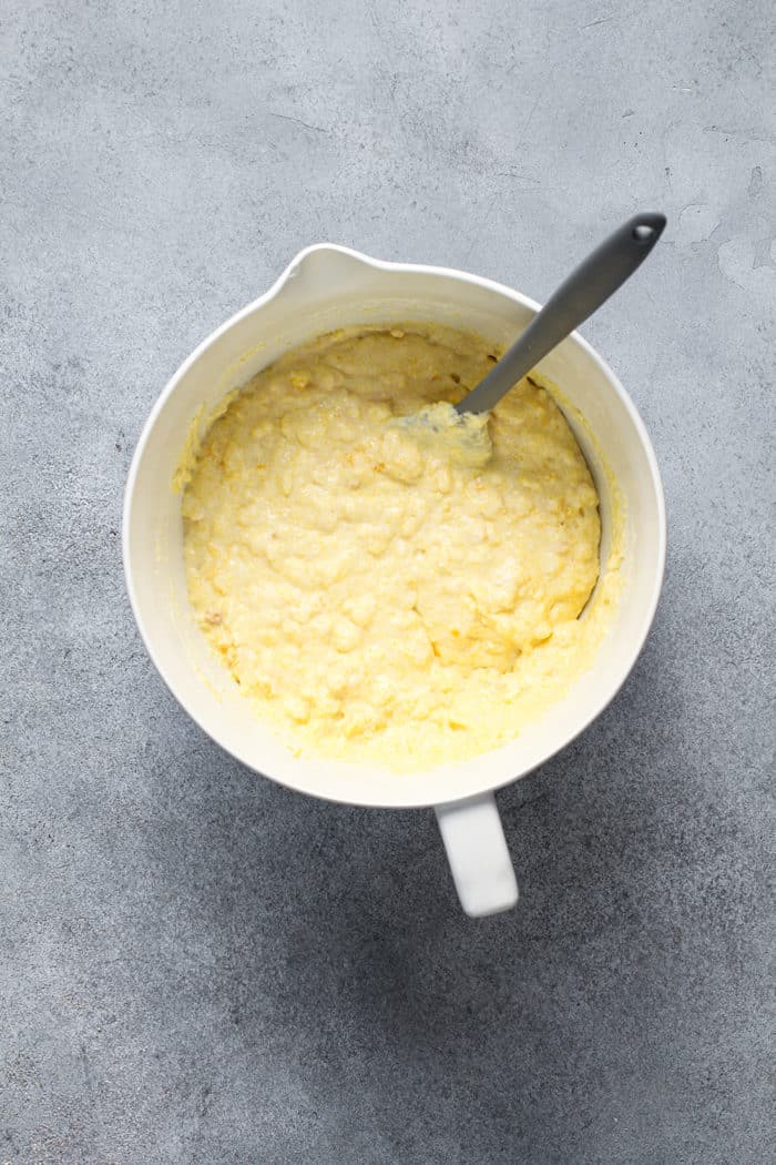 Spatula stirring together the batter for Jiffy corn casserole in a white mixing bowl