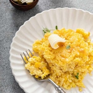 Fork next to a portion of jiffy corn casserole on a white plate