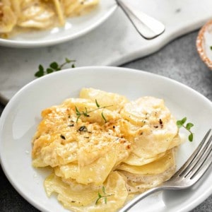 White plate with a serving of potato gratin. A second plate is in the background