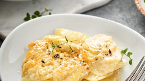 White plate with a serving of potato gratin. A second plate is in the background