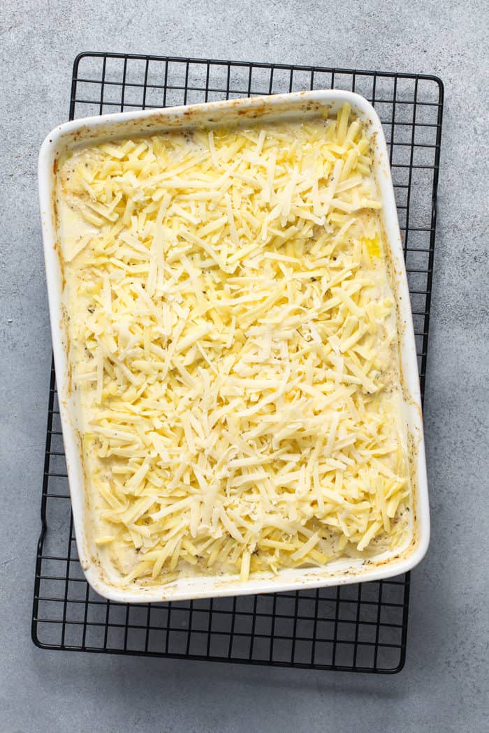 Shredded cheese on top of a baked potato gratin, ready to go under the broiler