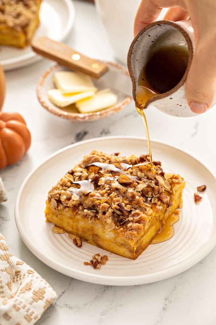 Syrup being poured over a slice of pumpkin french toast casserole on a white plate