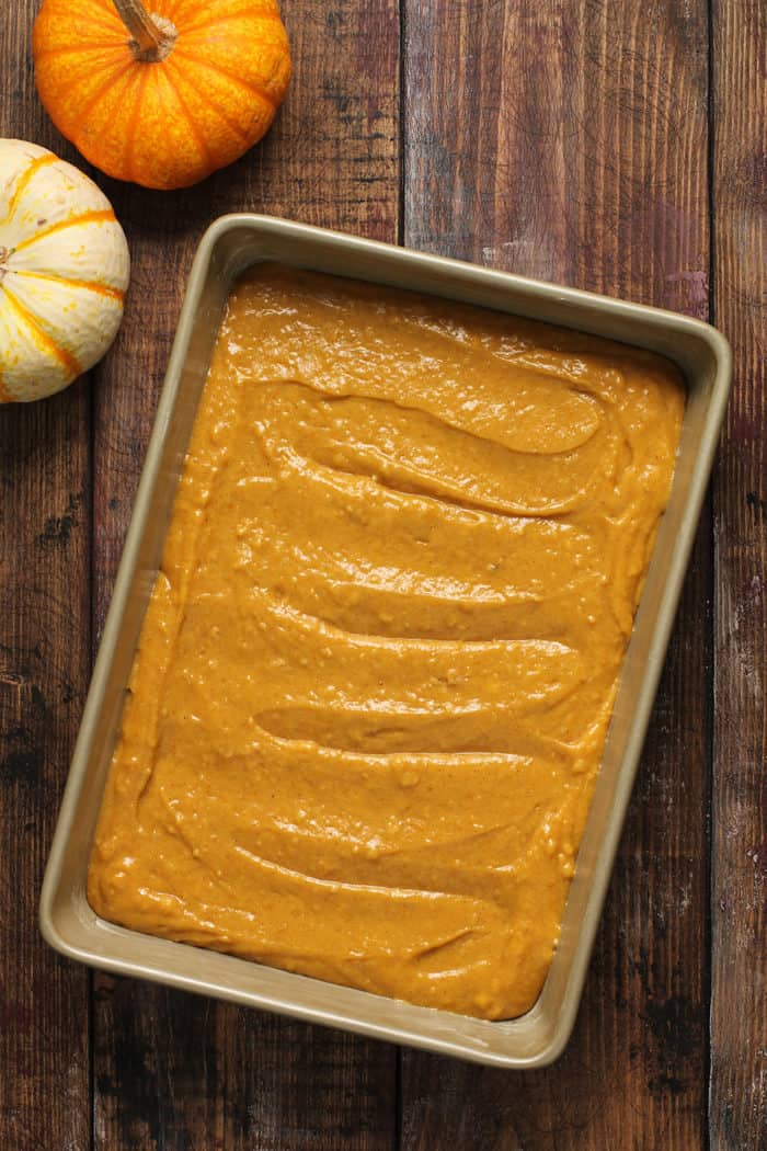 Pumpkin coffee cake batter in a metal cake pan set on a wooden table