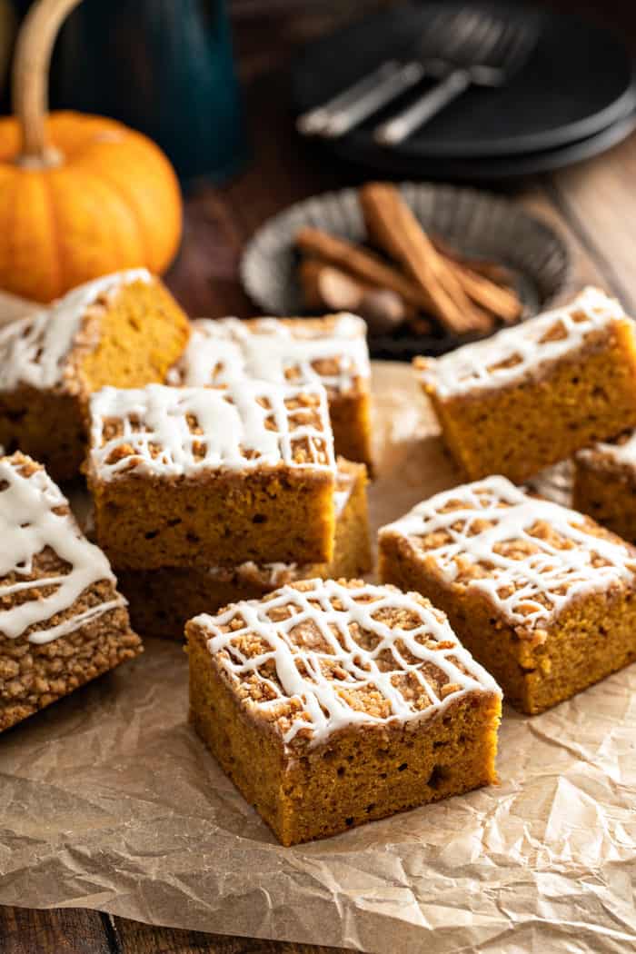 Several slices of pumpkin coffee cake, topped with drizzled icing, scattered on a piece of parchment paper
