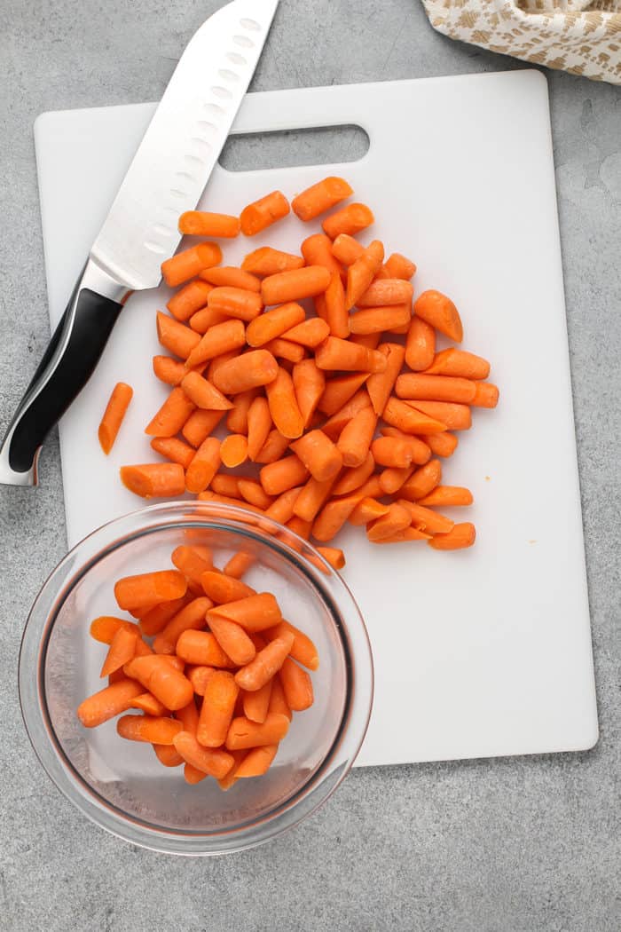 Baby carrots being cut in half on a white cutting board