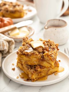 Stacked slices of pumpkin french toast casserole topped with butter and syrup on a white plate