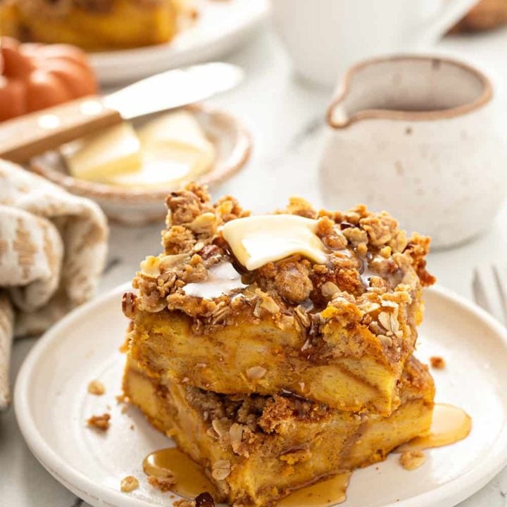 Stacked slices of pumpkin french toast casserole topped with butter and syrup on a white plate