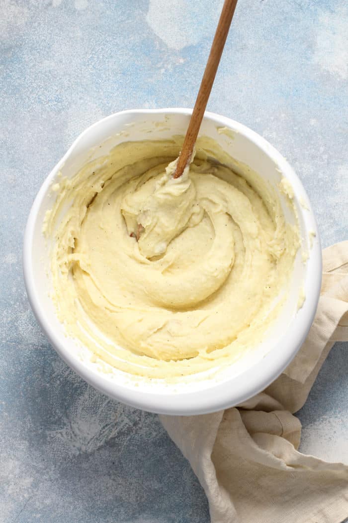 Wooden spoon stirring mashed potatoes in a white bowl