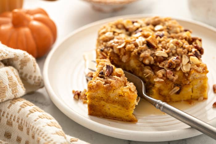 Fork cutting a bite of pumpkin french toast casserole, set on a white plate