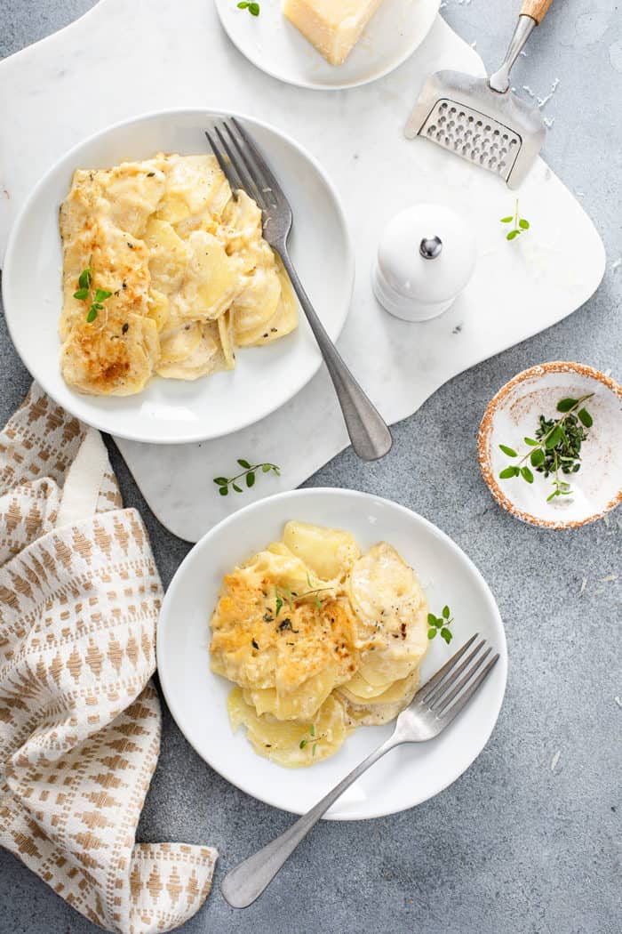 Overhead view of two white plates of potato gratin on a gray countertop