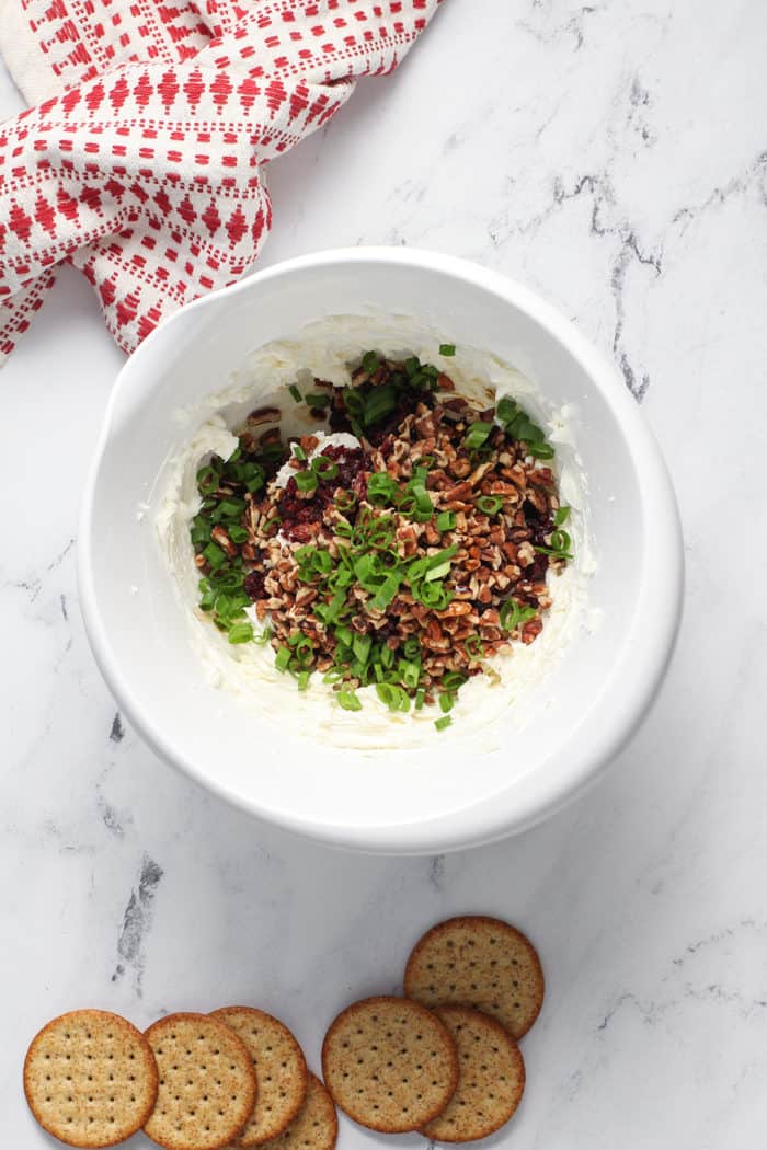 Pecans, cranberries, and green onions being added to a white mixing bowl