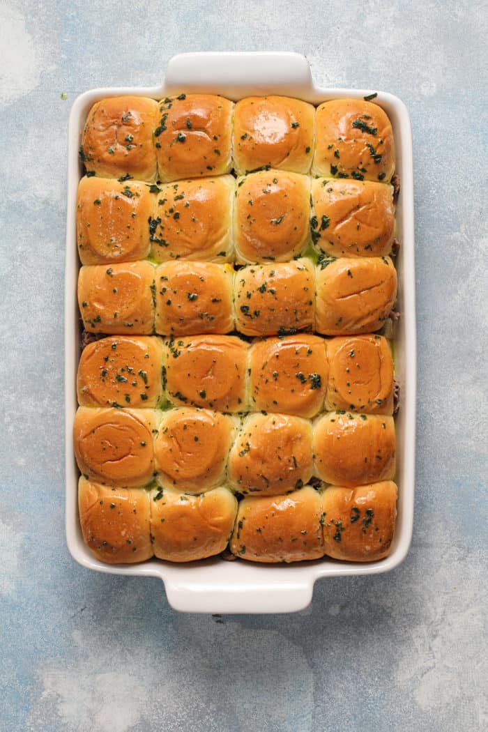 Fully assembled cheesesteak sliders, ready to bake, in a white baking dish