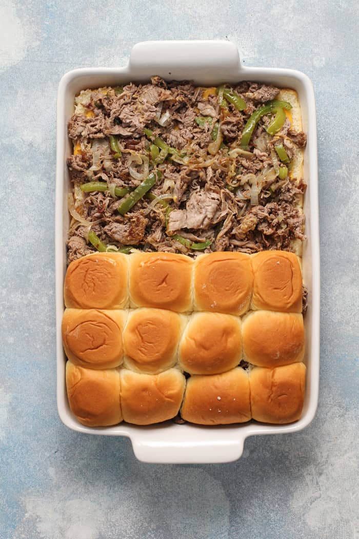 Philly cheesesteak sliders half assembled in a white baking dish