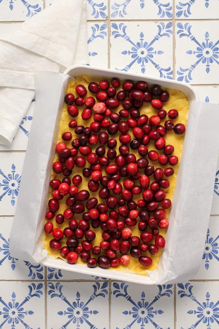 Whole cranberries on top of cake batter in a parchment-lined baking dish
