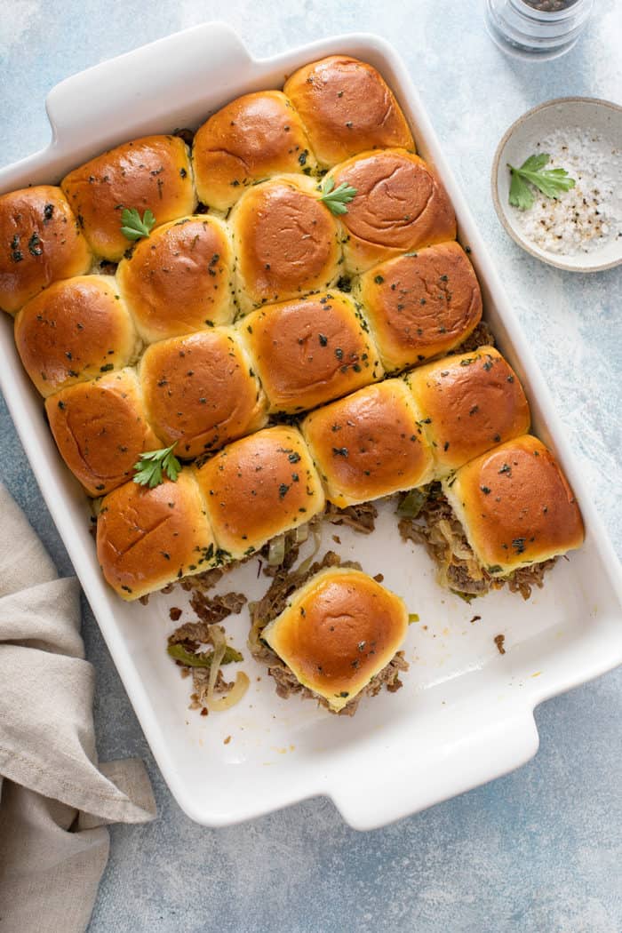 Overhead view of baked and sliced philly cheesesteak sliders in a white baking dish