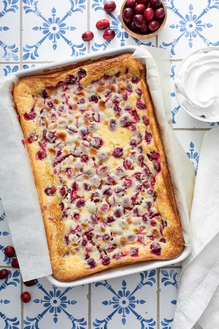 Baked gooey butter bars in a parchment-lined baking dish, set on a blue and white tiled table