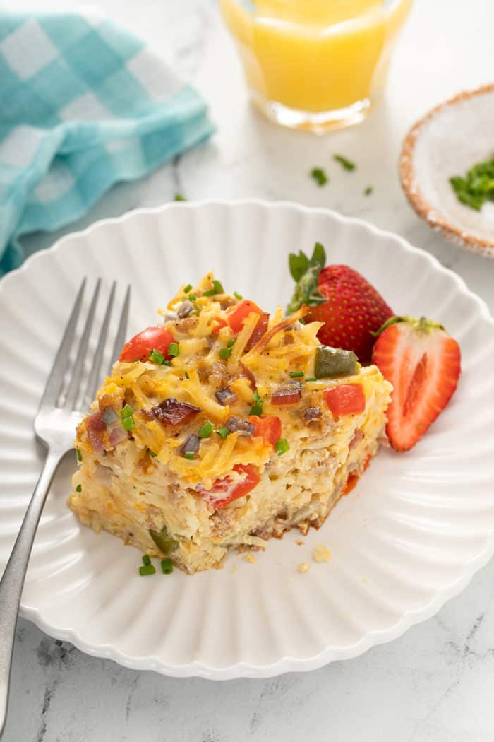 Piece of hash brown breakfast casserole with a bite taken out of it on a white plate next to a fork