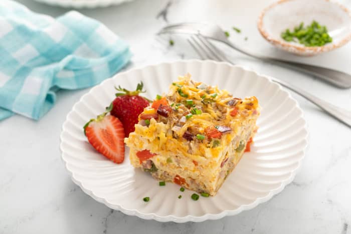 Slice of hash brown breakfast casserole set next to strawberries on a white plate