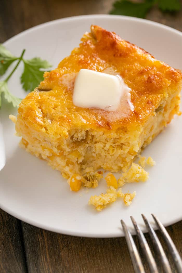 Close up of a pice of corn casserole with a bite taken from the corner on a white plate