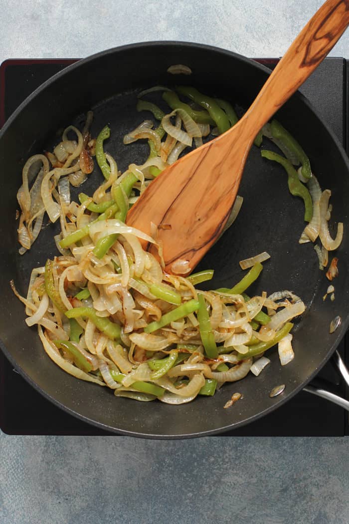 Wooden spoon stirring cooked onions and peppers in a skillet