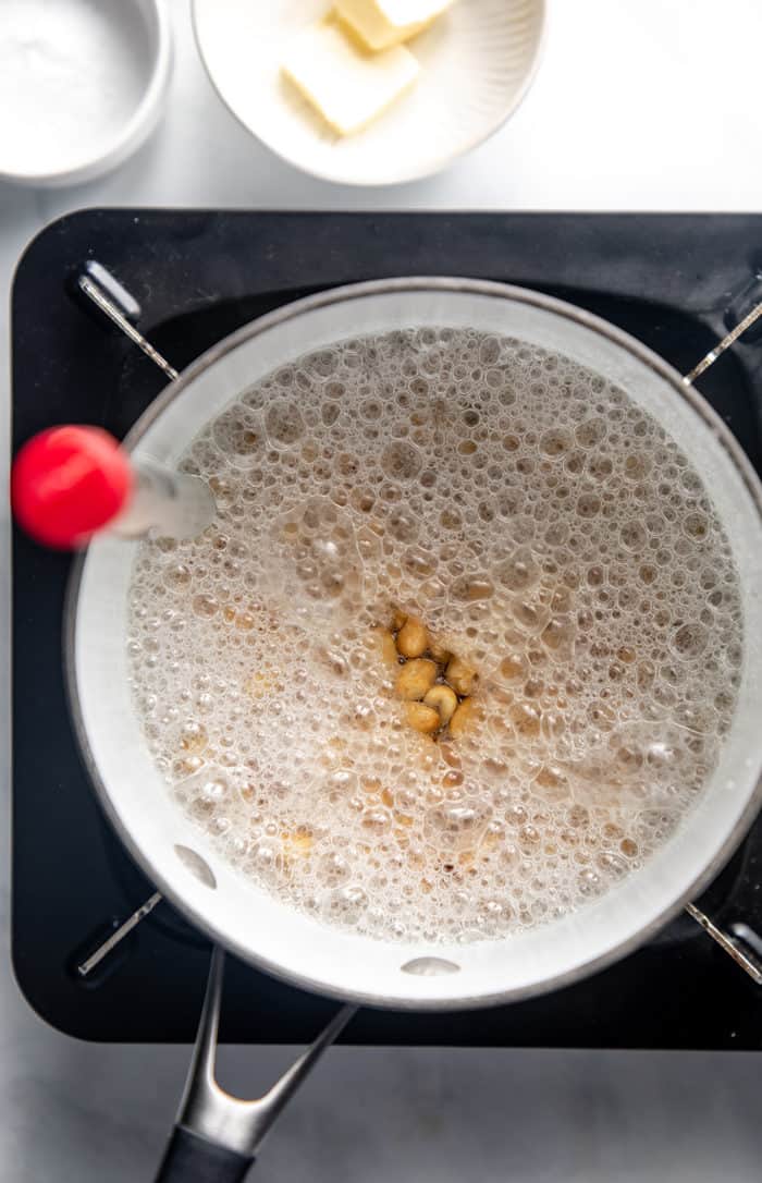 Peanut brittle starting to cook in a saucepan with a candy thermometer