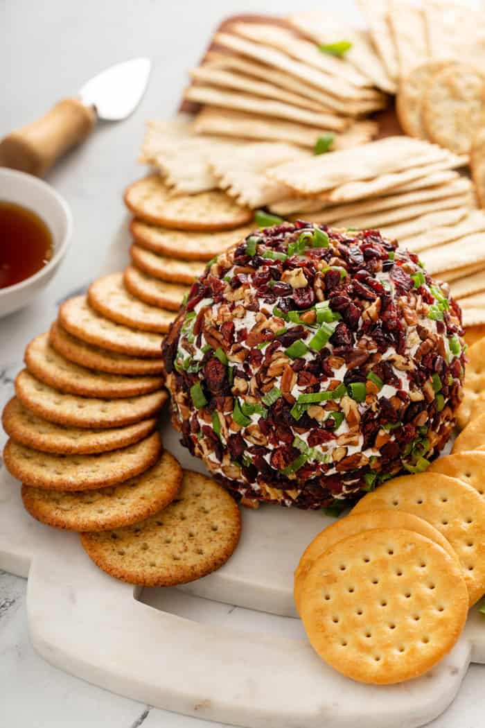 Cranberry goat cheese ball set on a board with crackers around it