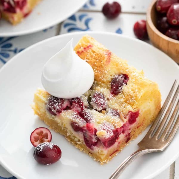 Close up of a cranberry gooey butter bar, topped with whipped cream, on a white plate