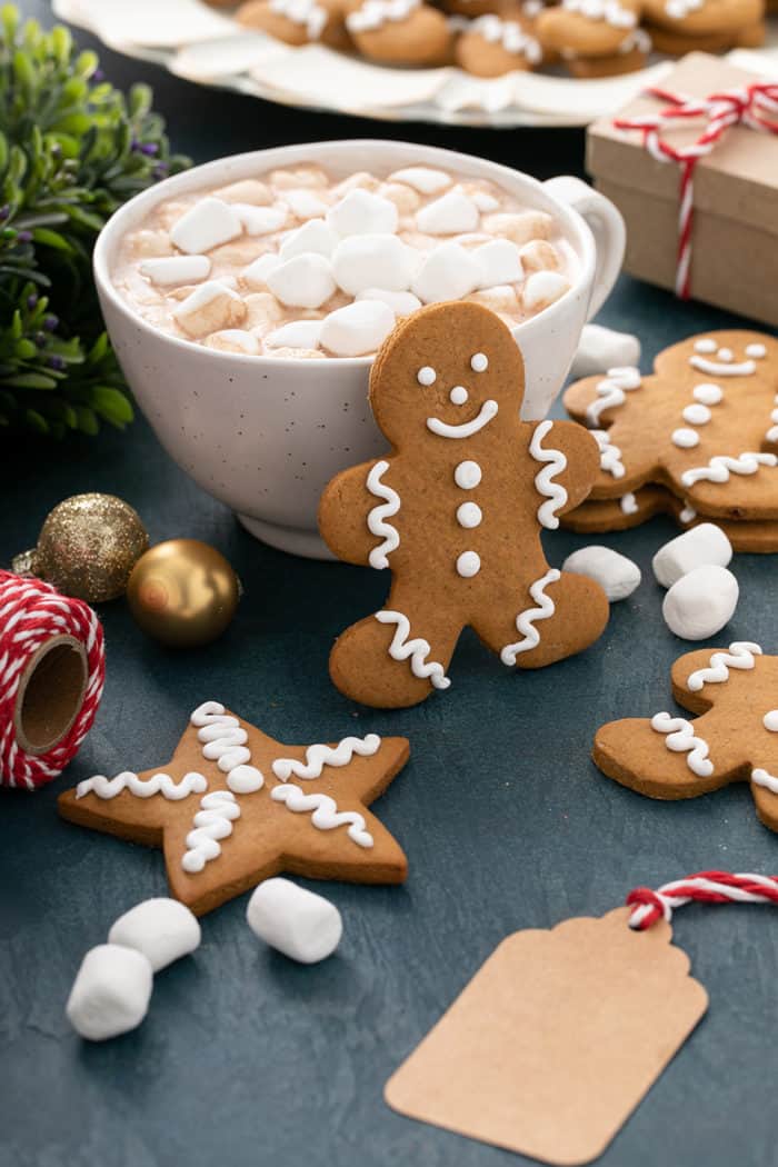 Cutout and iced gingerbread man cookie propped up against a mug of hot chocolate