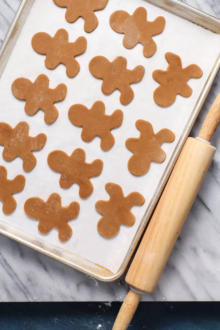 Cutout gingerbread man shapes on a parchment lined baking sheet