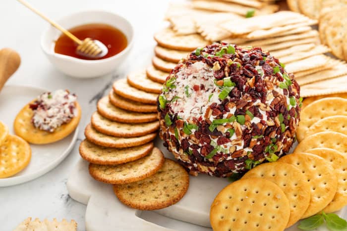 Cranberry Pecan Goat Cheese Ball with some of it taken out of it, set on a platter surrounded by crackers