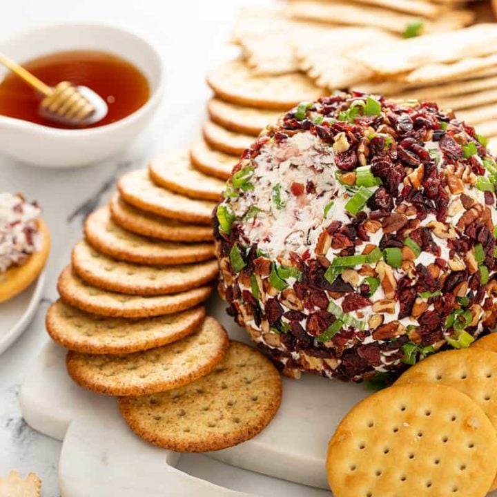 Cranberry Pecan Goat Cheese Ball with some of it taken out of it, set on a platter surrounded by crackers