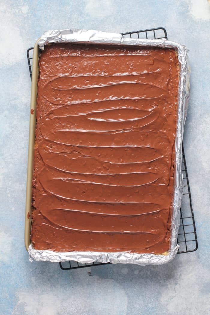 Melted chocolate spread on top of saltine toffee in a foil-lined sheet pan