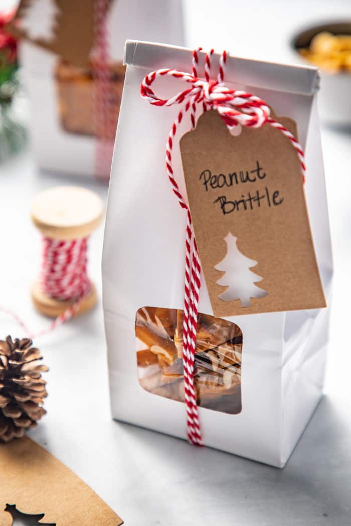 Close up of a white package filled with peanut brittle. The package is tied with red and white twine and has a tag that reads "peanut brittle"