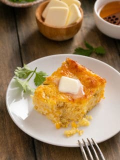 Slice of green chile corn casserole on a white plate, with a bite taken out of the corner of the casserole