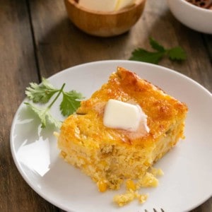 Slice of green chile corn casserole on a white plate, with a bite taken out of the corner of the casserole