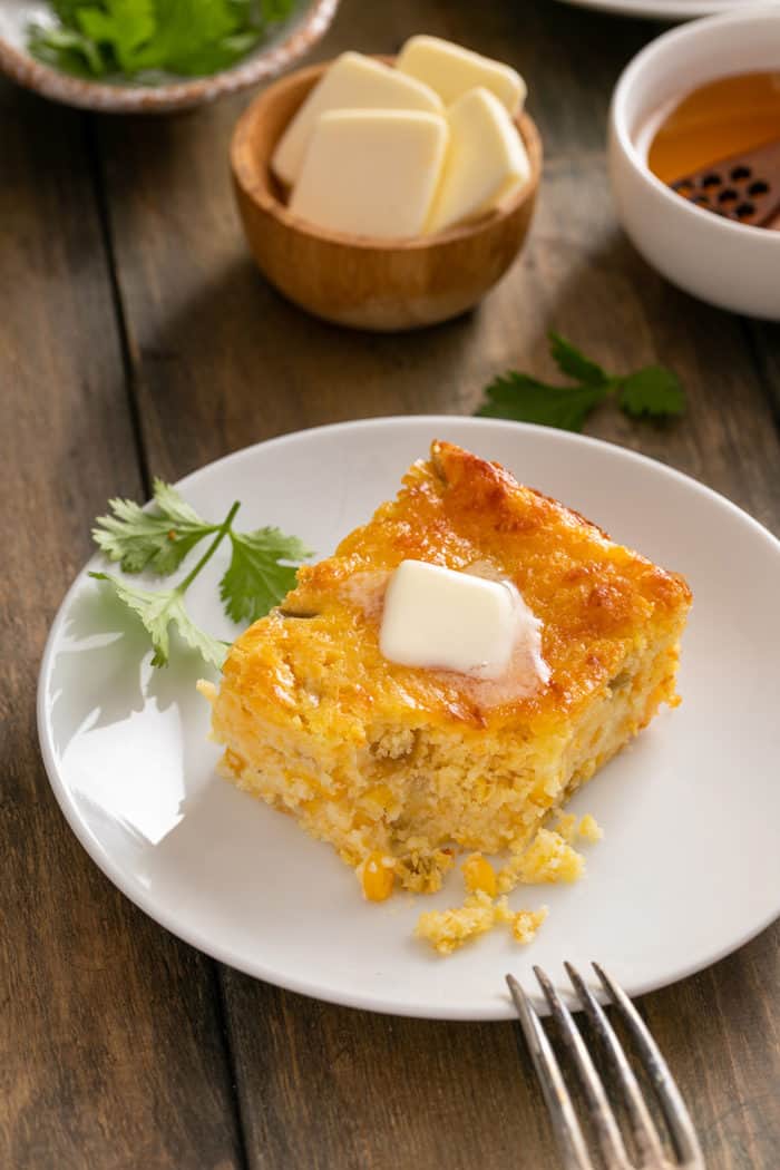 Slice of green chile corn casserole on a white plate, with a bite taken out of the corner of the casserole