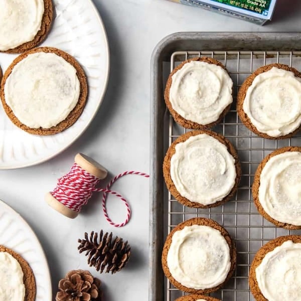 Baking sheet with frosted ginger cookies next to plates of frosted ginger cookies