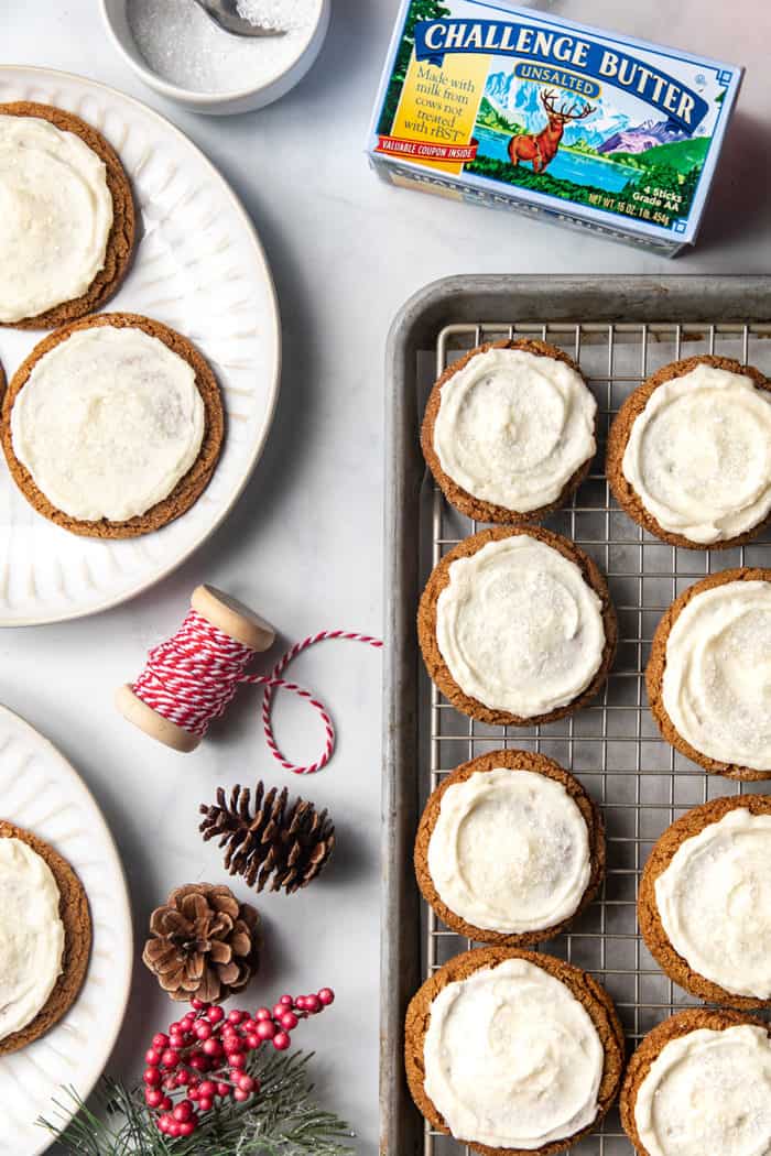 Baking sheet with frosted ginger cookies next to plates of frosted ginger cookies