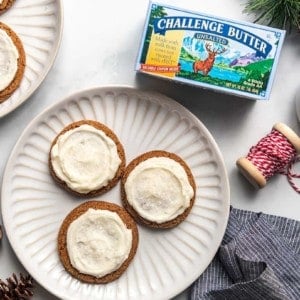 Overhead view of a plate of three frosted ginger cookies next to a package of butter