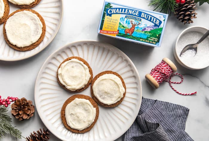 Overhead view of a plate of three frosted ginger cookies next to a package of butter