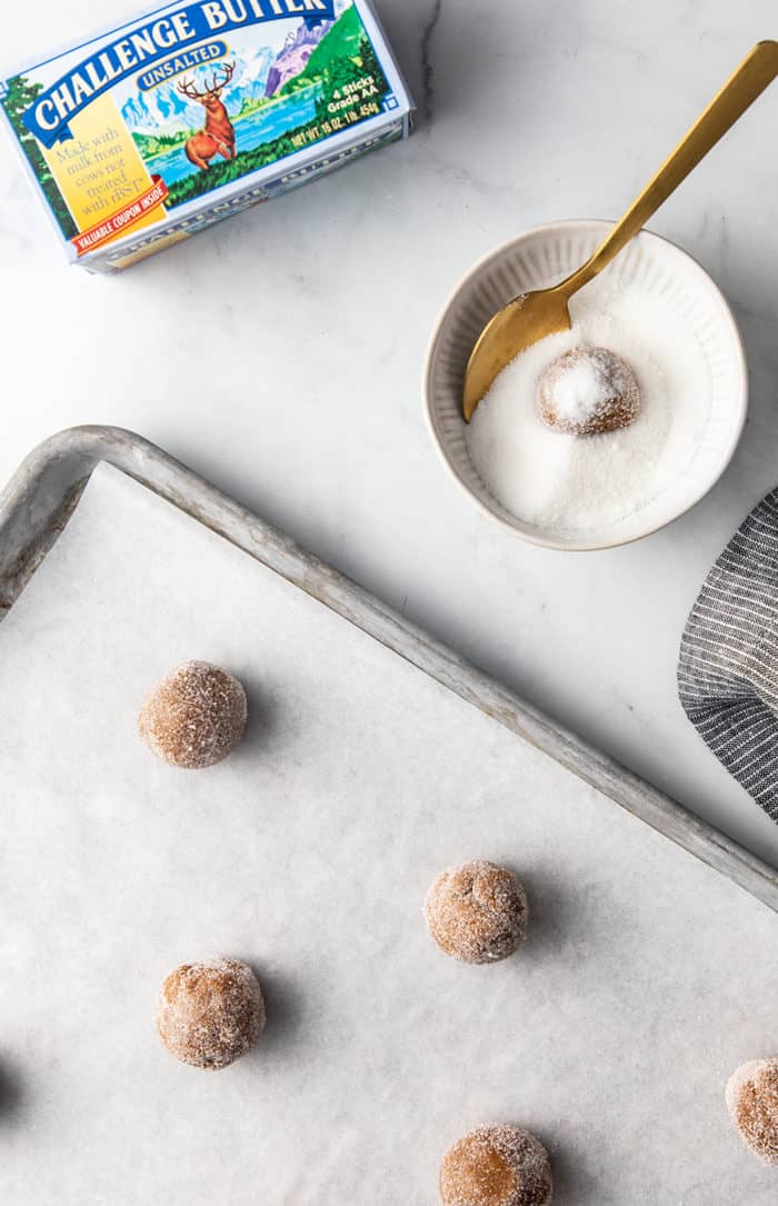 Ginger cookie dough balls being rolled in granulated sugar